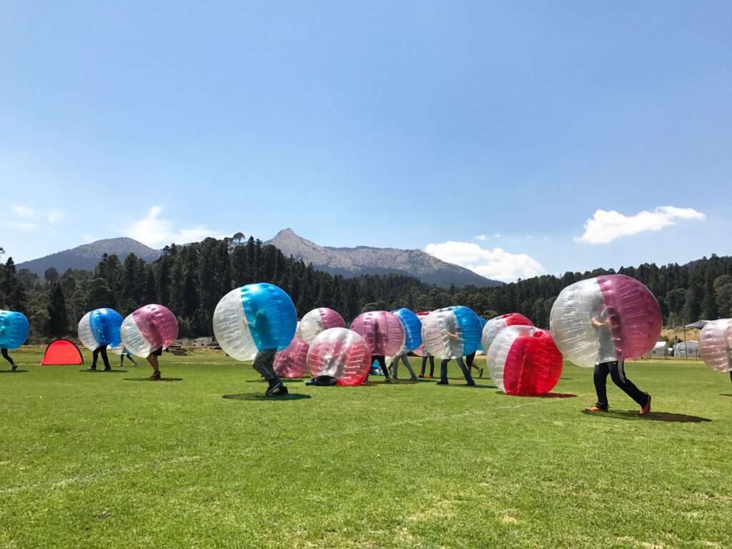 Personas jugando futbol en amplio jardín con vista del cerro del Ajusco de fondo.