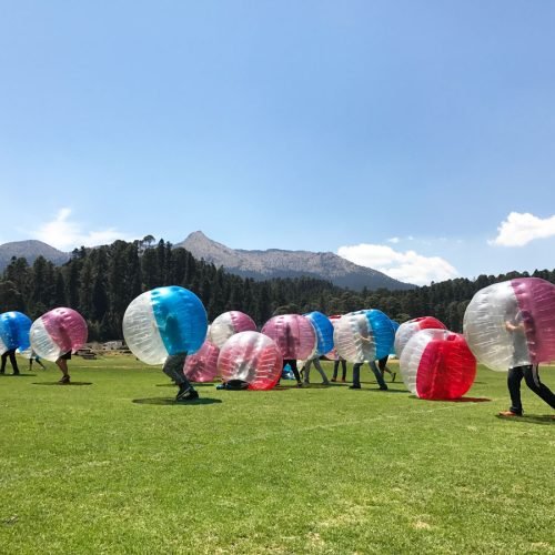 Personas jugando futbol en amplio jardín con vista del cerro del Ajusco de fondo.